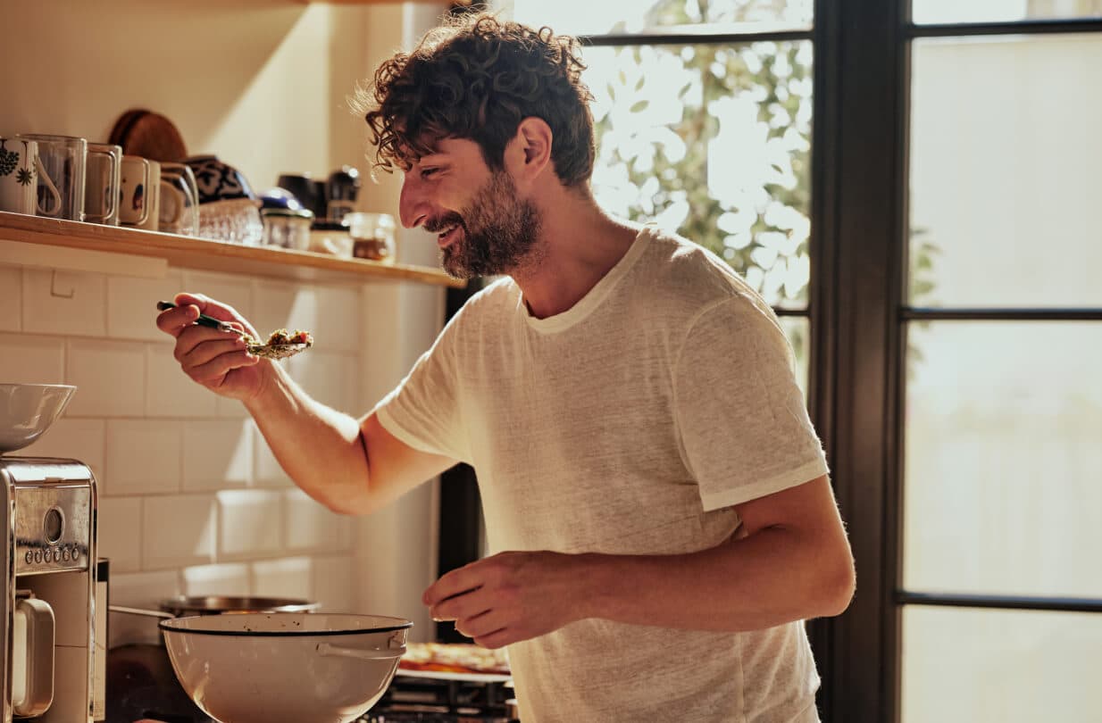 Happy man eating pasta in a sunlight kitchen