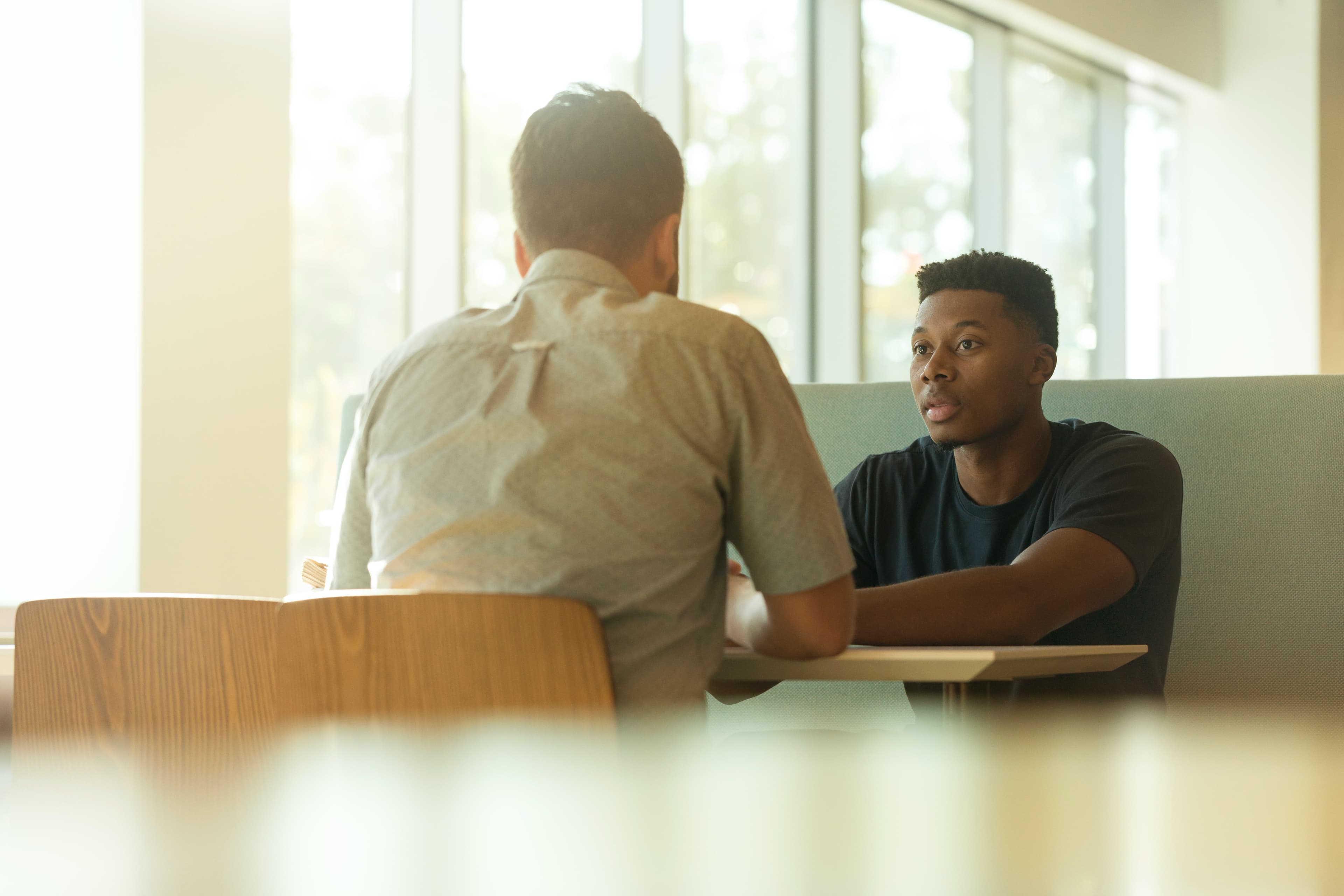 Two young men are sitting at a table having a discussion.