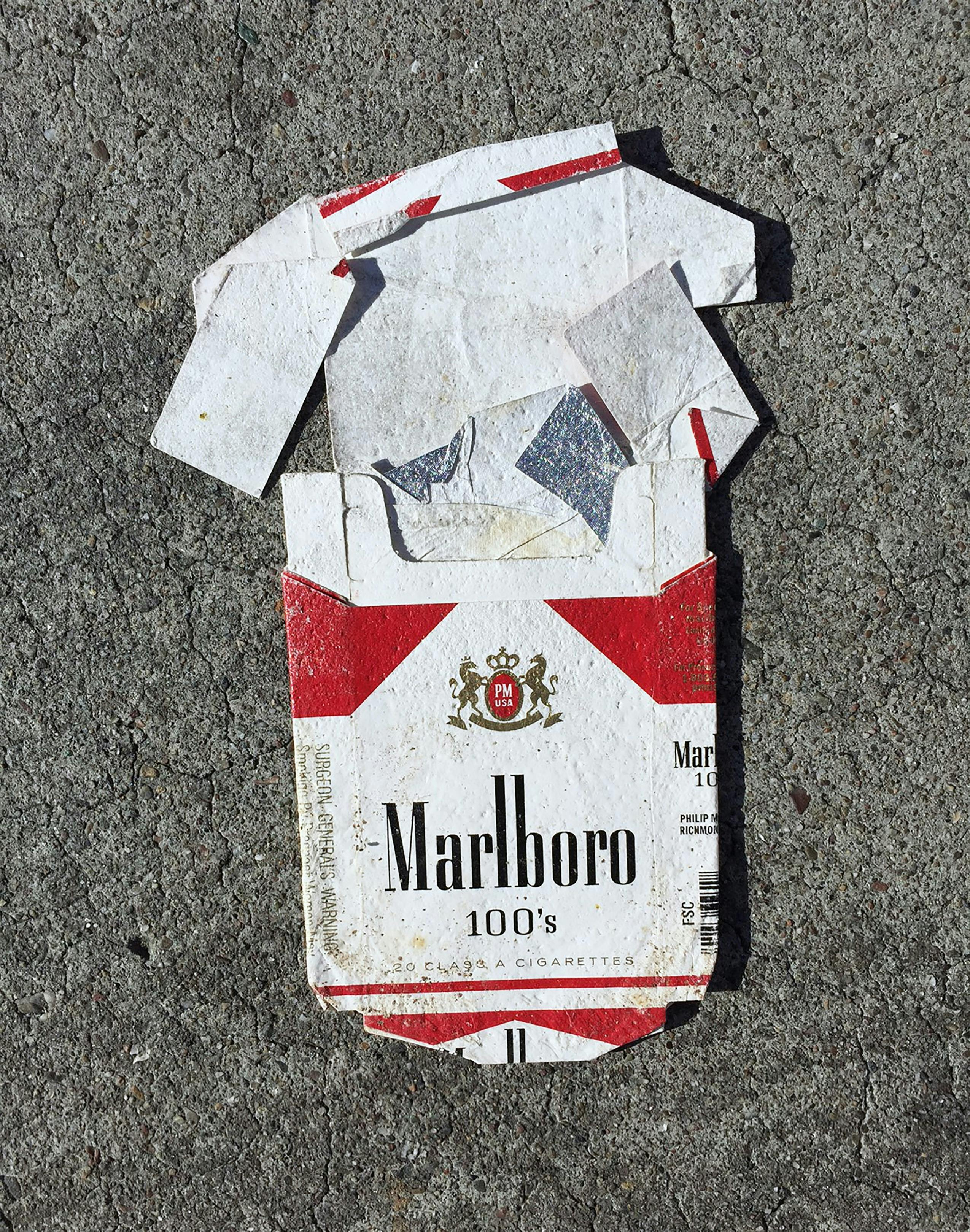 Close-up of a flattened, dirty pack of Marlboro cigarettes on the ground.
