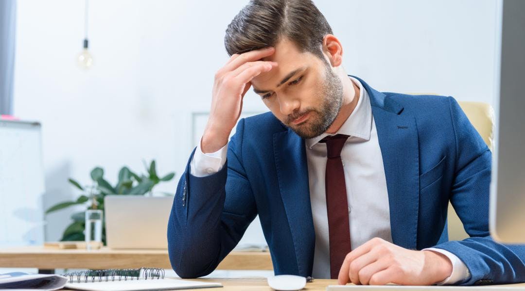 A worried business person looking down at their work desk with one hand on their head.