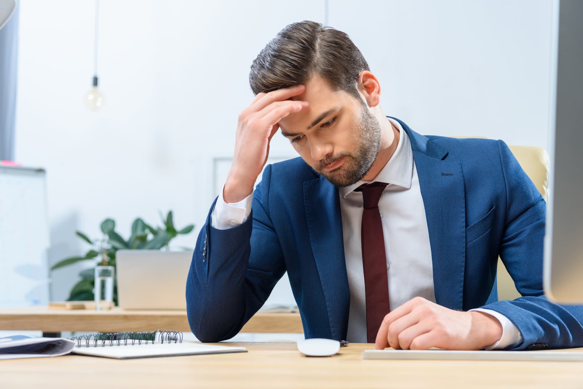 A worried business person looking down at their work desk with one hand on their head.
