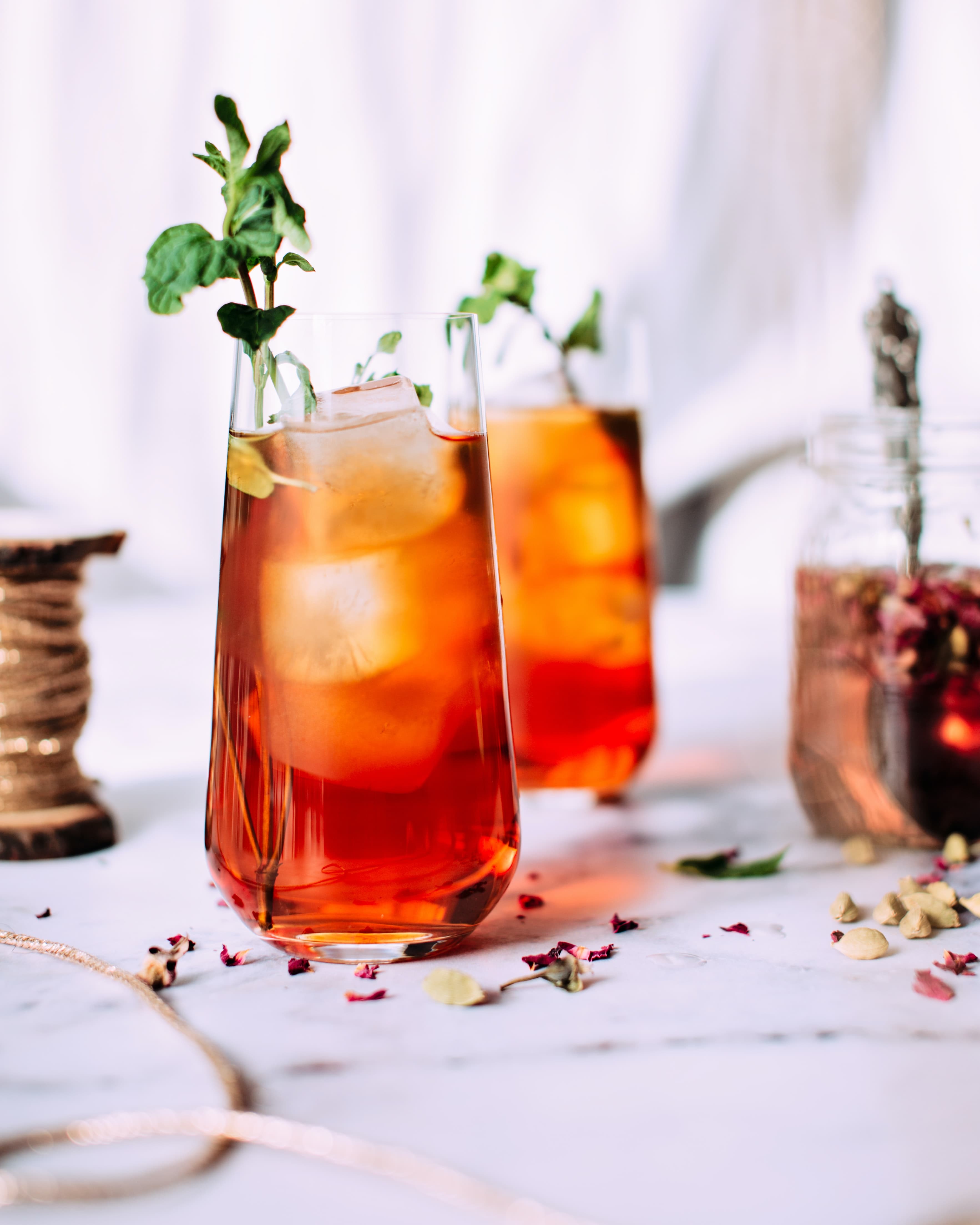 A close up of two cocktails with ice and a sprig of herbs in clear, slim glasses.