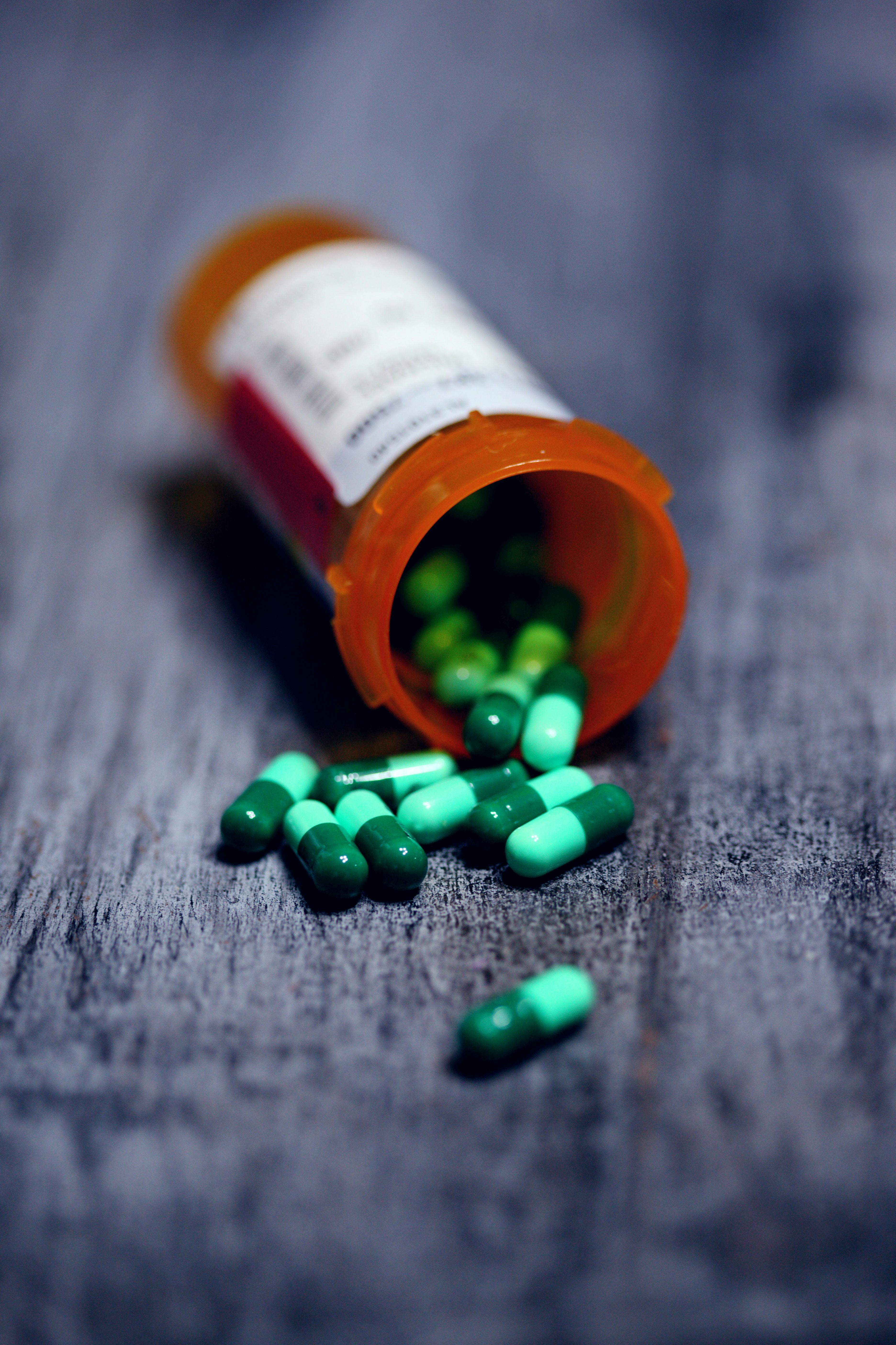An orange prescription lying on its side, with green capsules spilling out onto the ground.