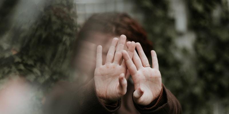 An out-of-focus close-up of a woman with her hands covering her face.