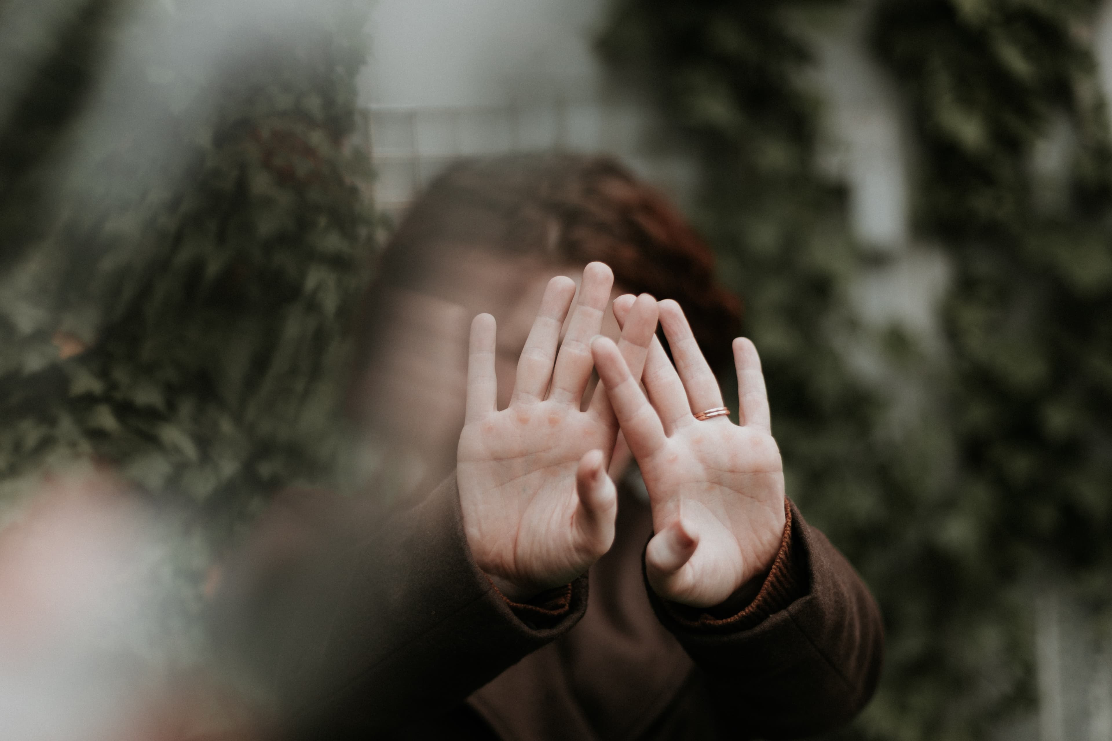 An out-of-focus close-up of a woman with her hands covering her face.