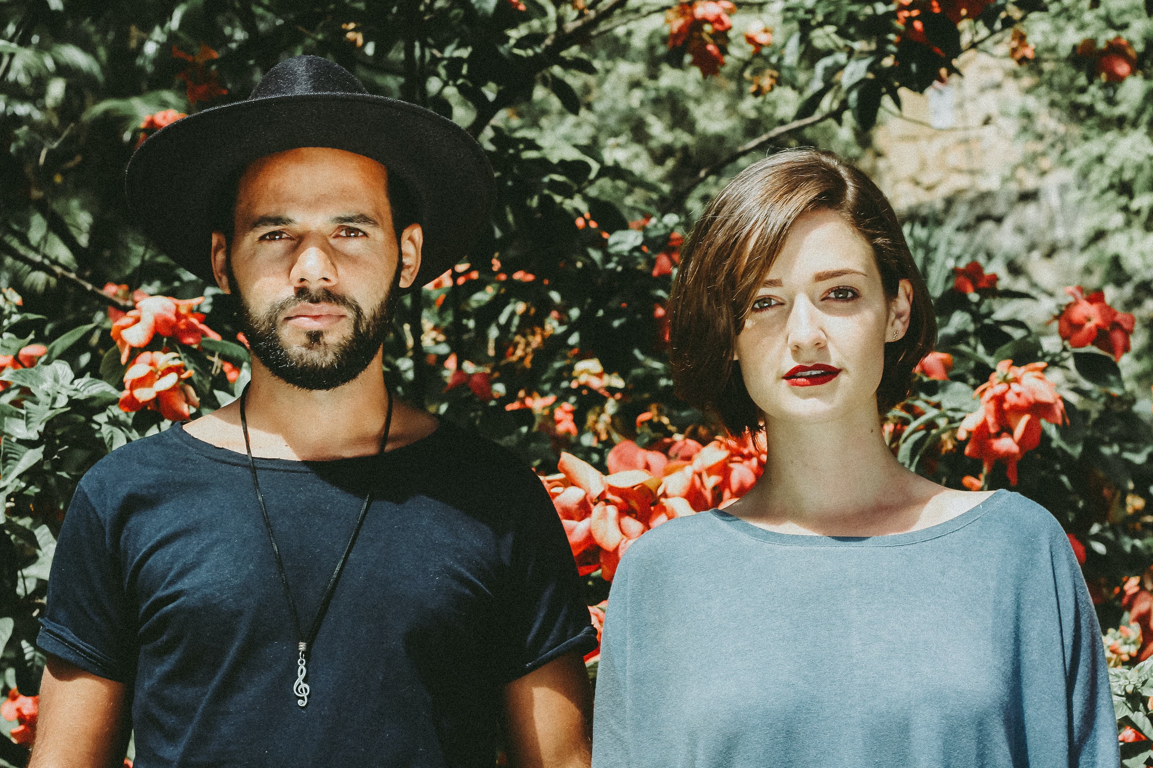 A couple staring straight ahead, surrounded by red flowers.