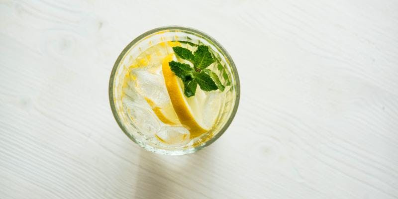 An aerial view of a glass of water garnished with a lemon wedge and herb.