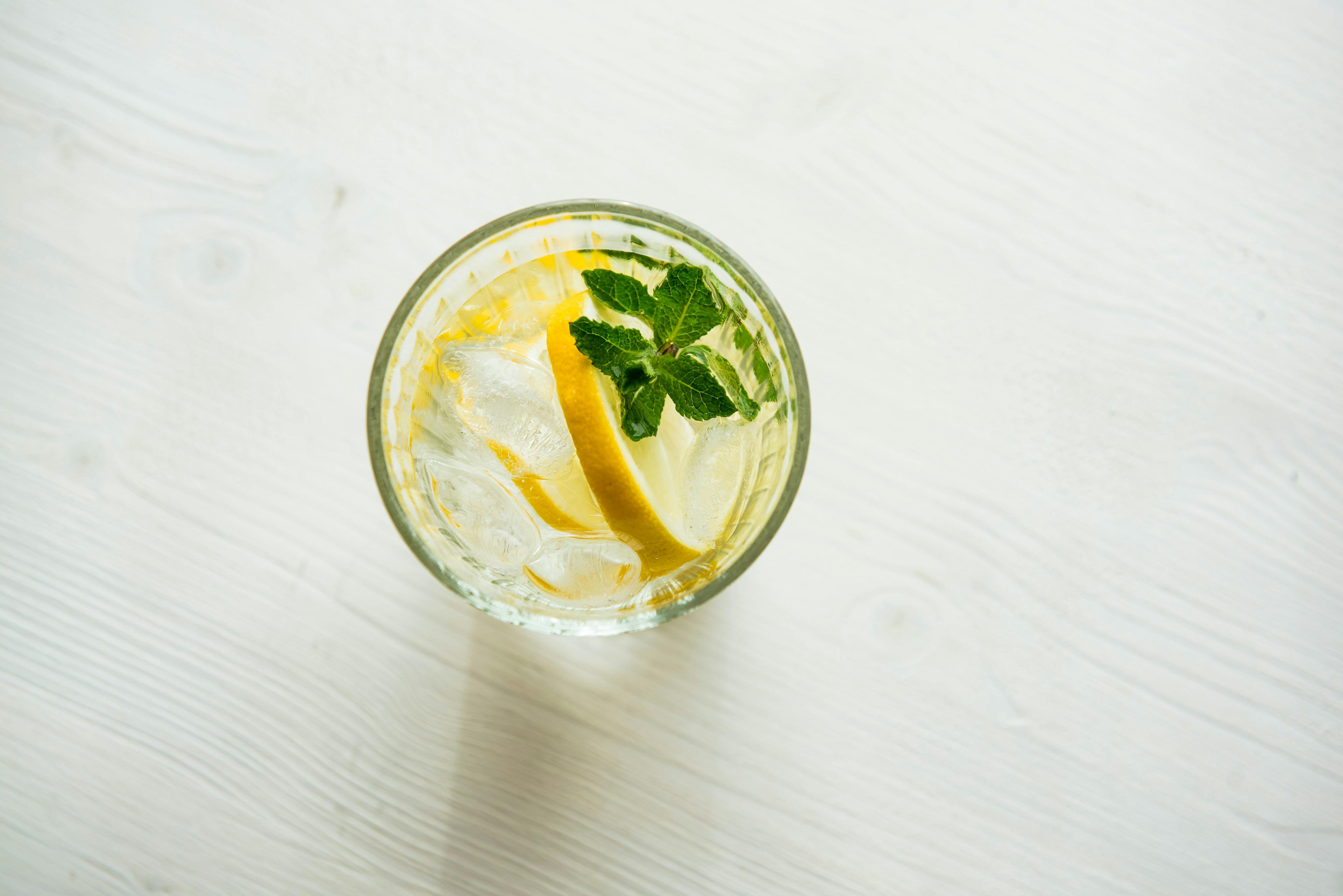 An aerial view of a glass of water garnished with a lemon wedge and herb.