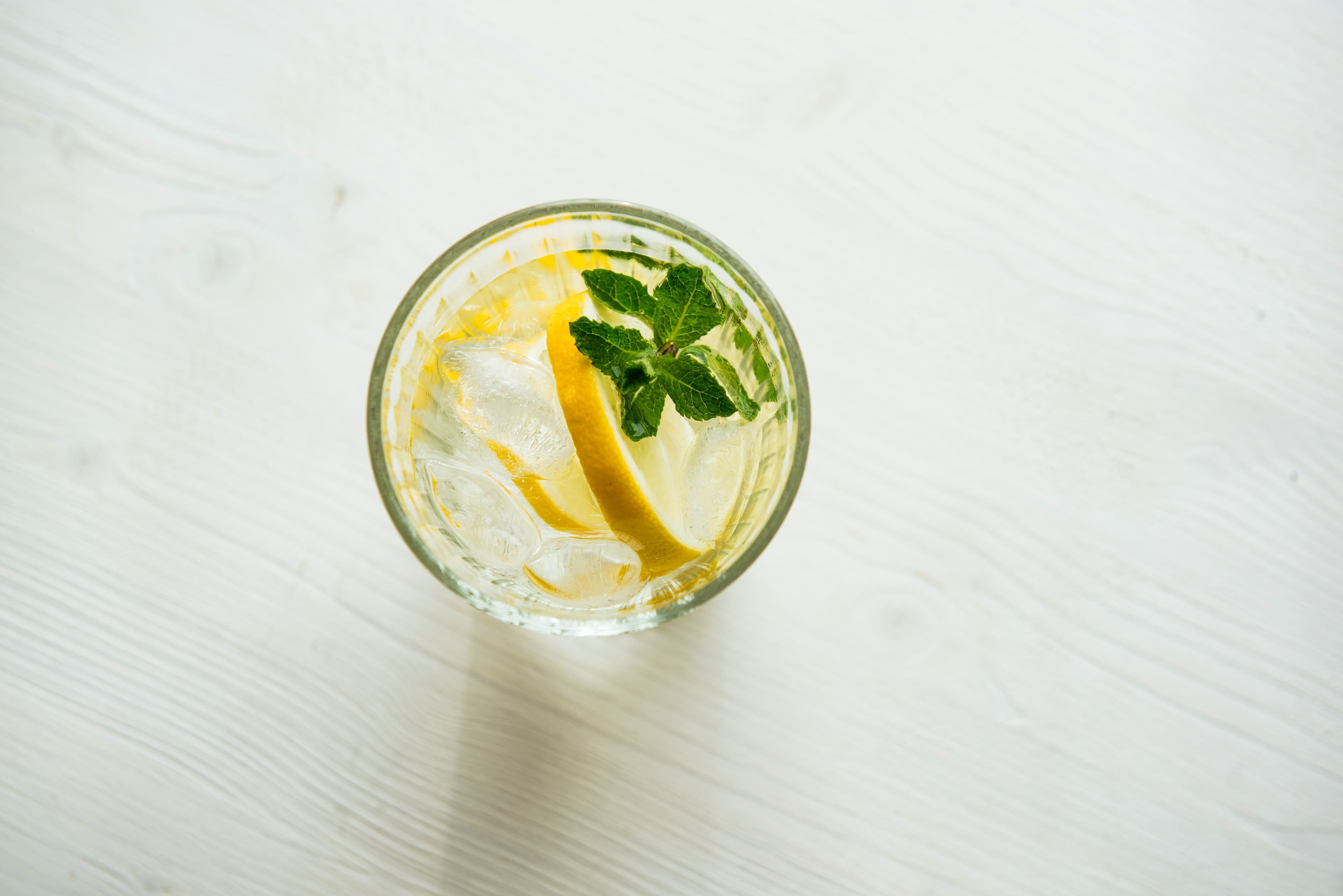 An aerial view of a glass of water garnished with a lemon wedge and herb.