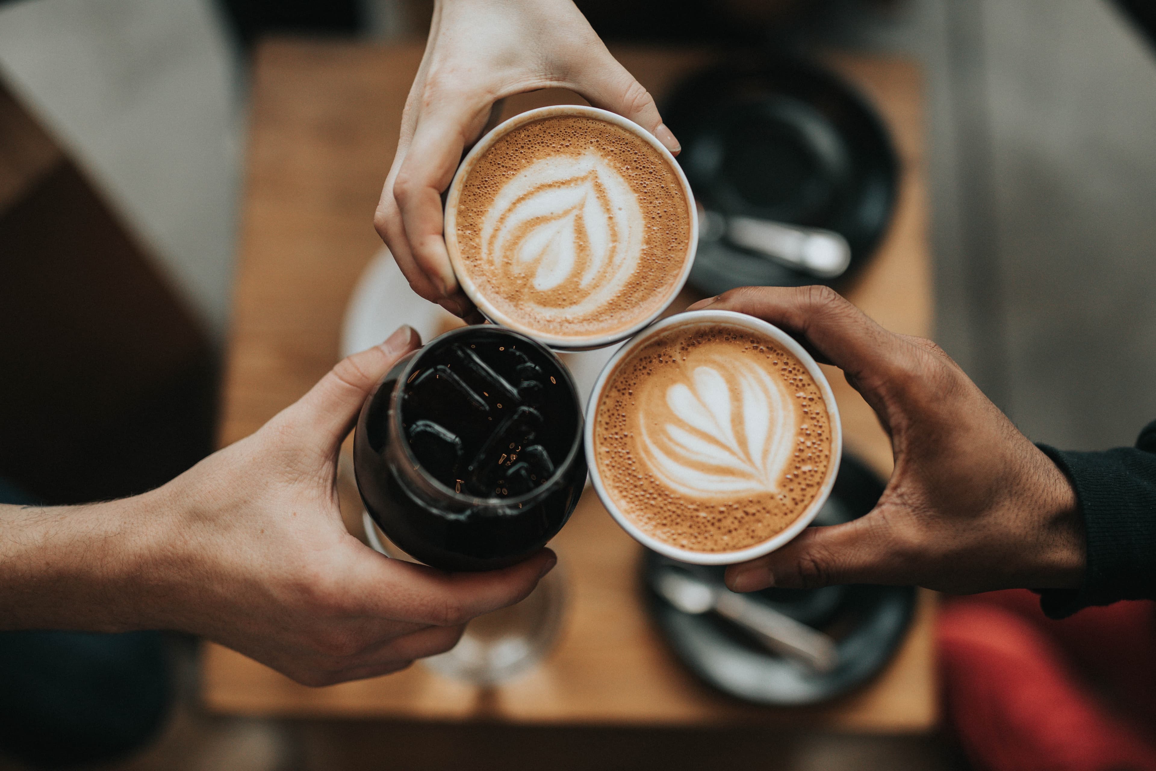 Close-up of three hands clinking cups of coffee together.