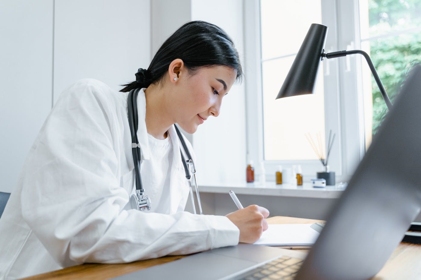 Female doctor making notes at desk in front of computer
