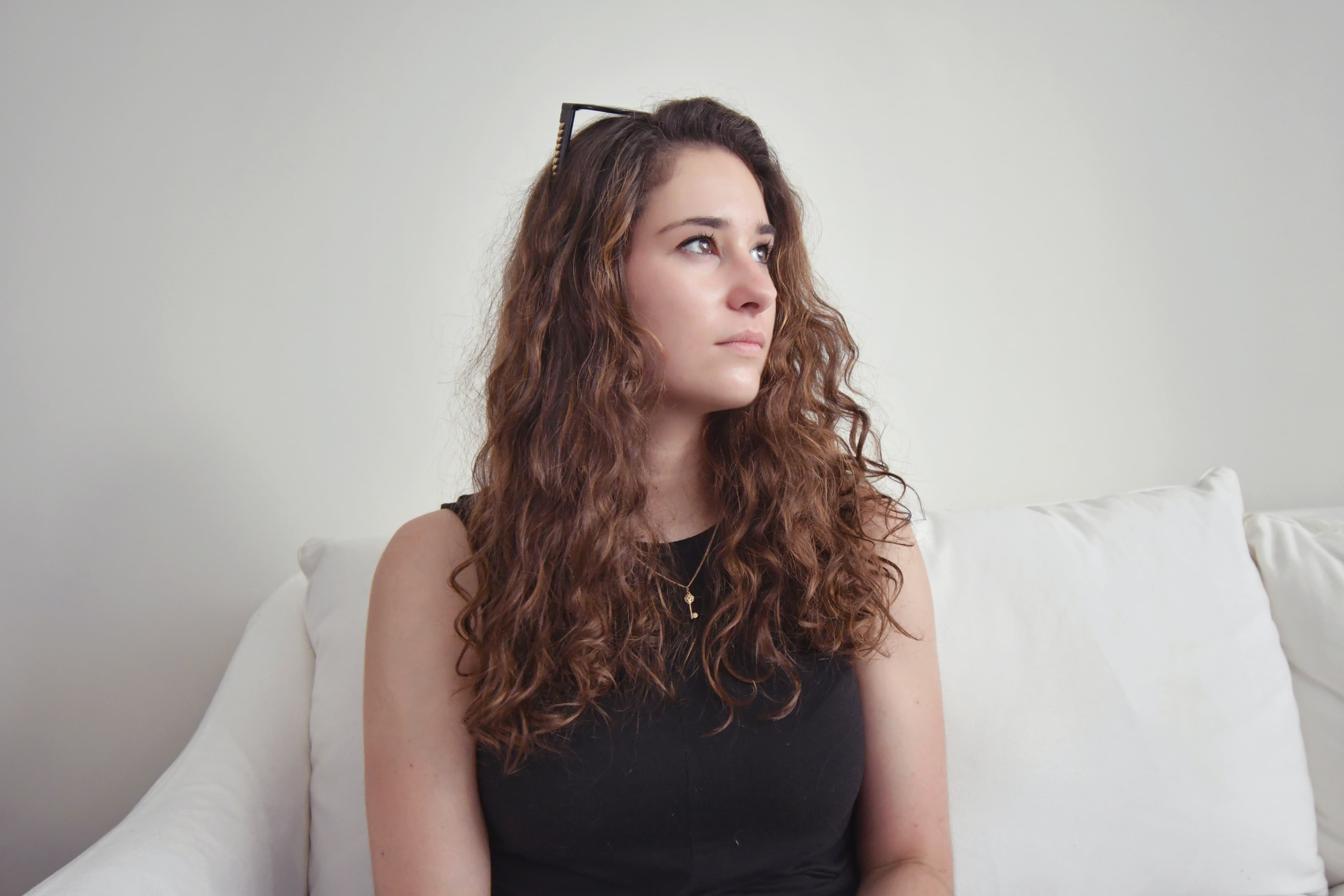 A person with curly hair sitting and staring off somberly to the right.