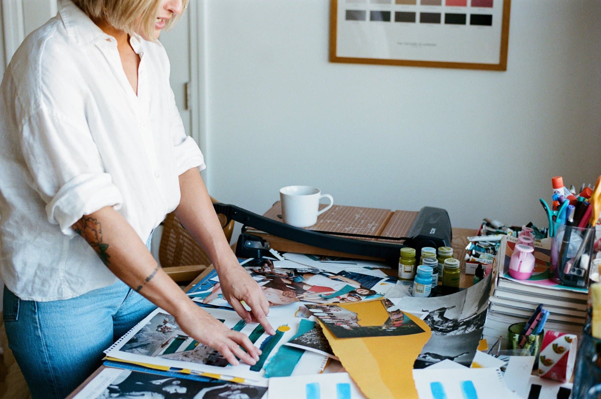A woman making a collage at a table, cutting and arranging paper.