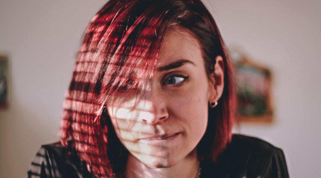 A person with bright red hair looking contemplative.