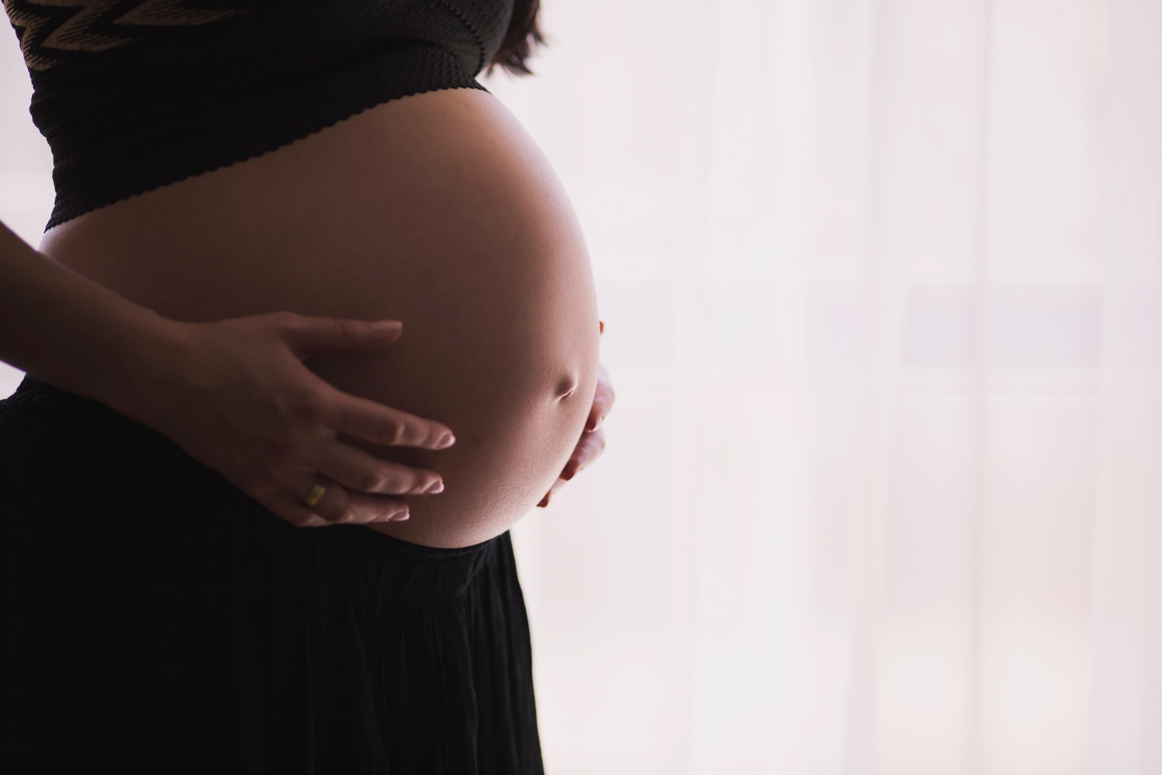 Close-up photo of pregnant woman's torso. She is wearing a short black top and black sweatpants, and resting her hands on her bare belly.