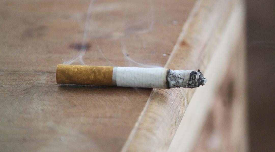 A lit cigarette rests on the edge of a table.