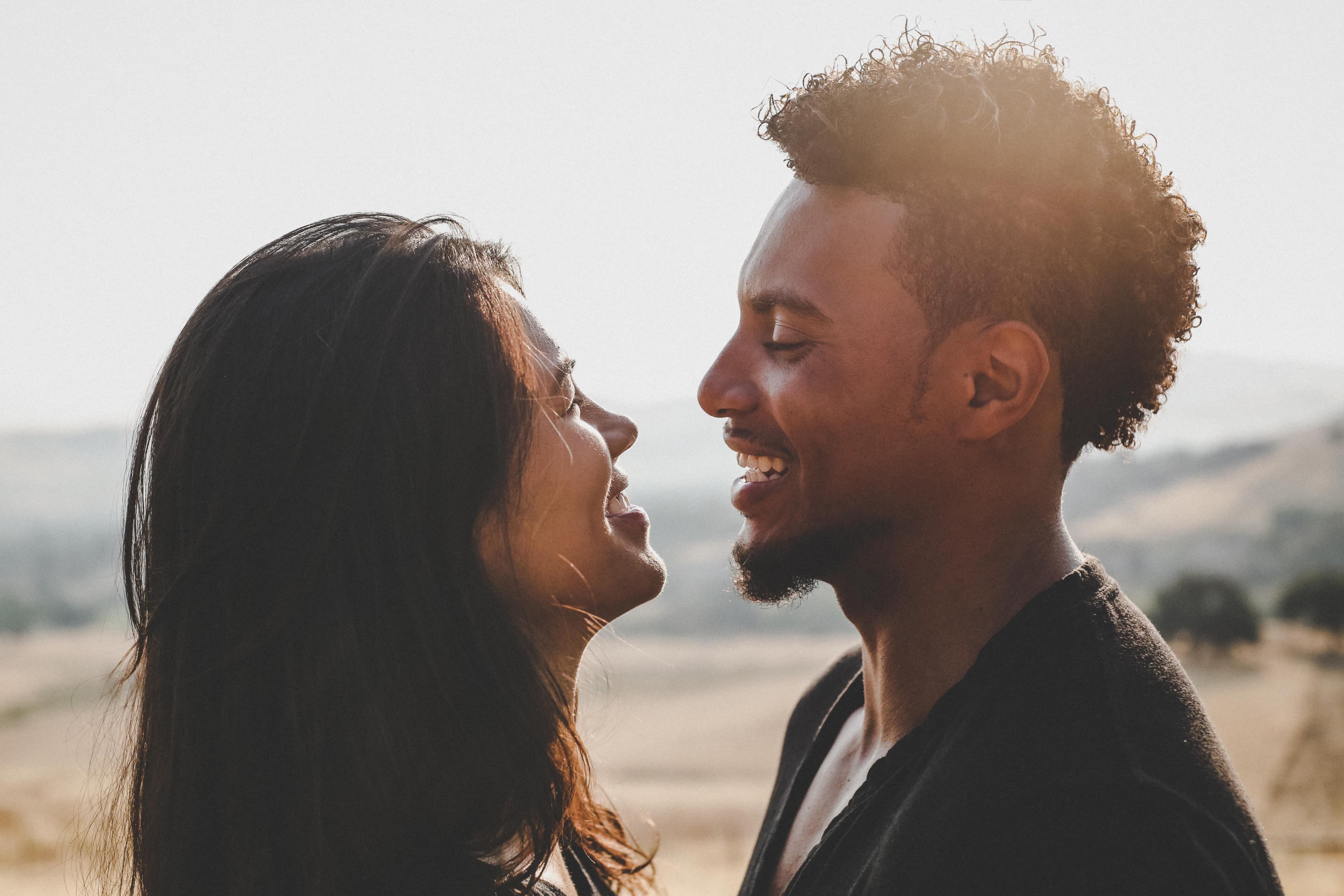 Close-up of an East Asian woman and a Black man standing facing each other, with big smiles on their faces.