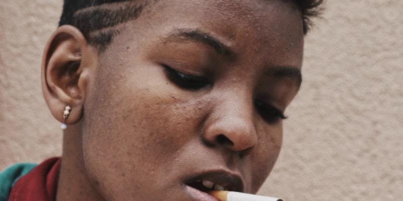 A close-up of a Back woman with short hair lighting a cigarette.