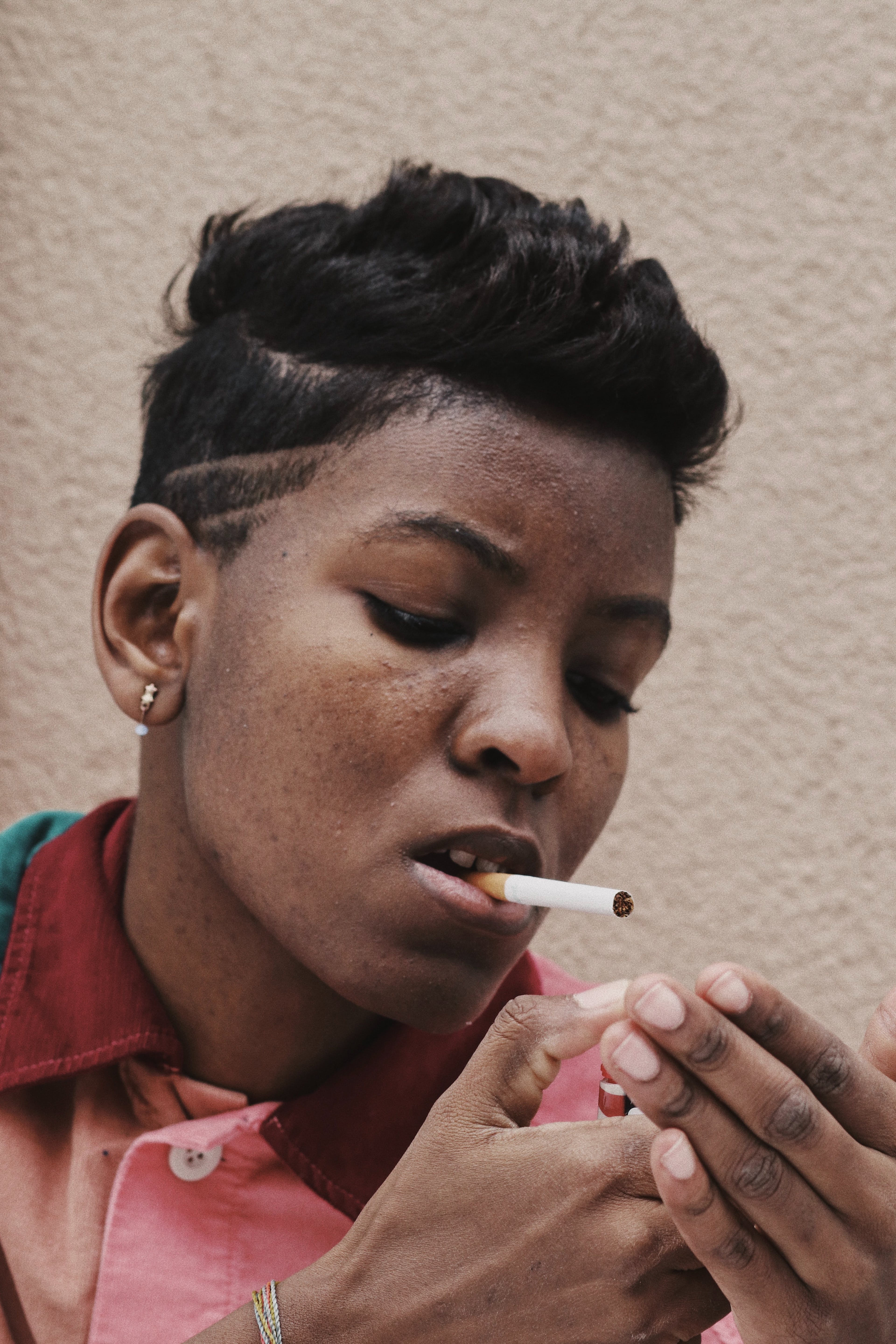 A close-up of a Back woman with short hair lighting a cigarette.