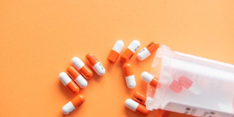 A pill bottle spilled over on an orange background.