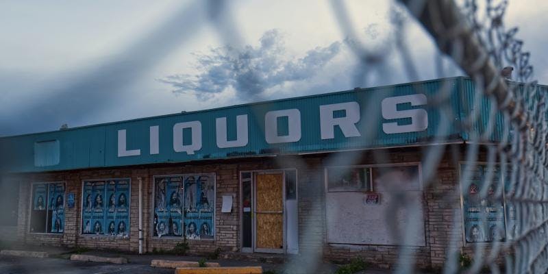 The outside of a liquor store is seen through a chain link fence.