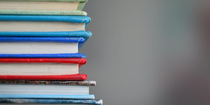 A close-up of six books with colored covers lying on their sides in a stack.