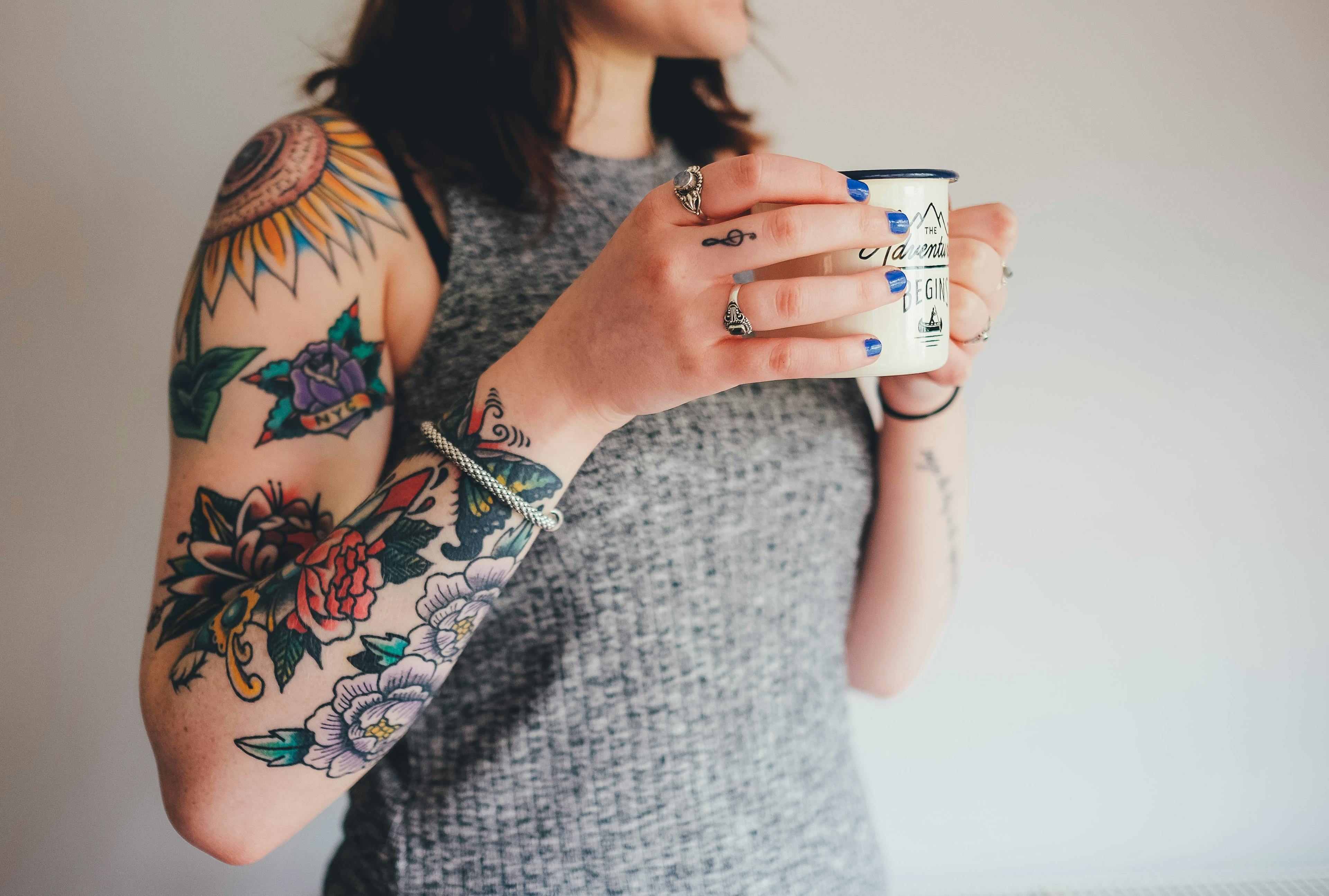 A person with a heavily tattooed arm, holding up a cup of coffee.