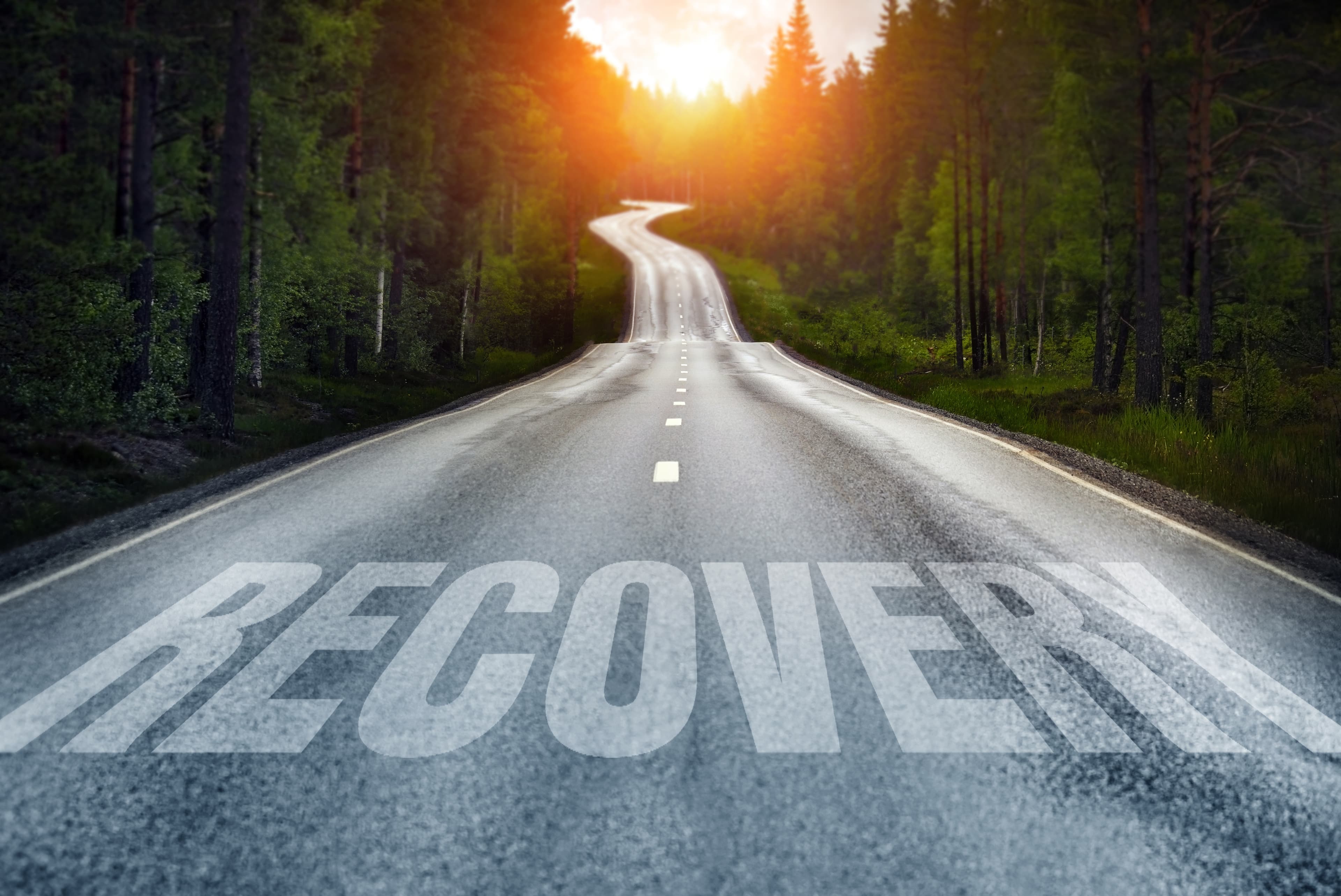 A country road at sunrise with the word "recovery" painted on it