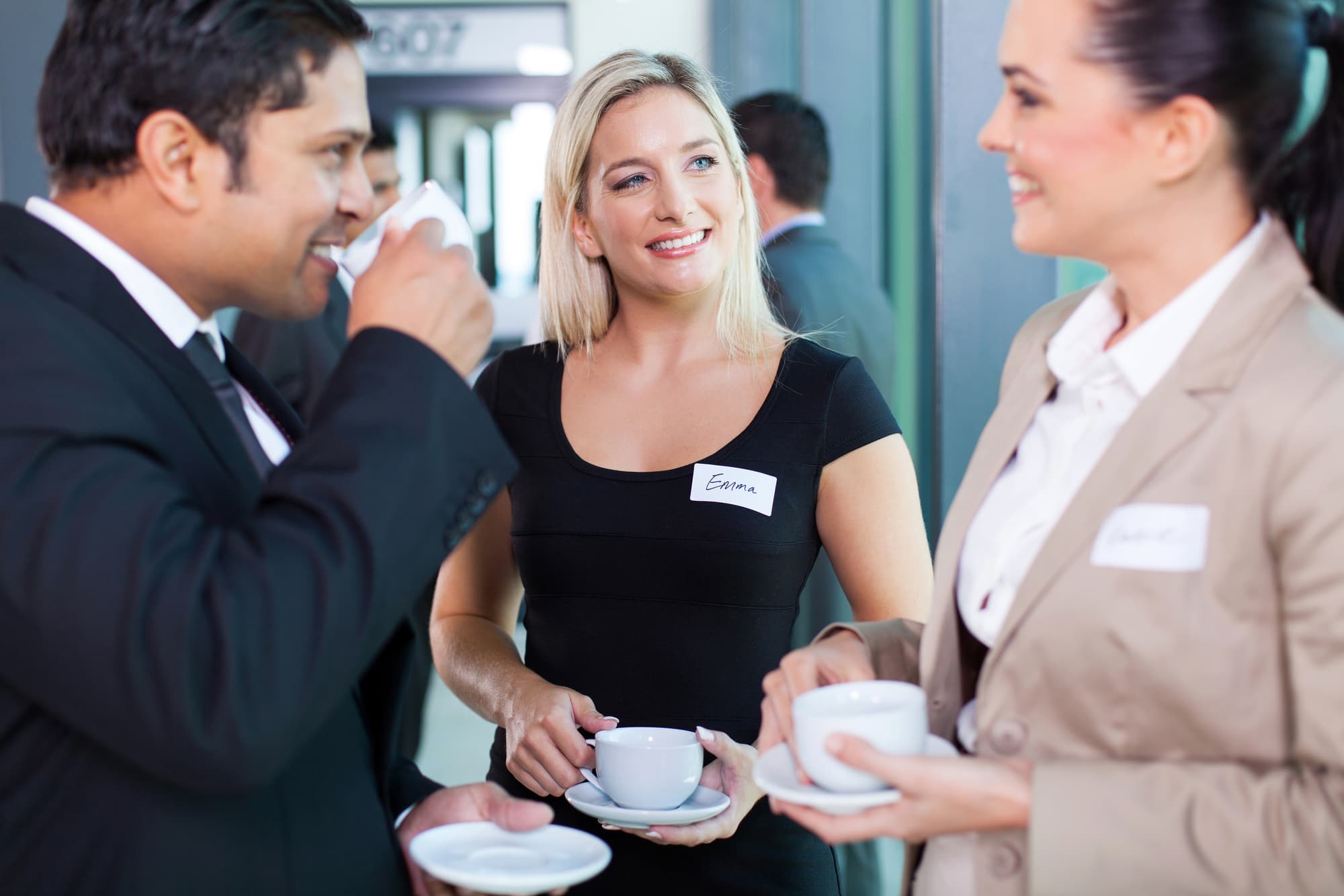 3 people with name tags chatting at a business networking event, holding and drinking coffee.