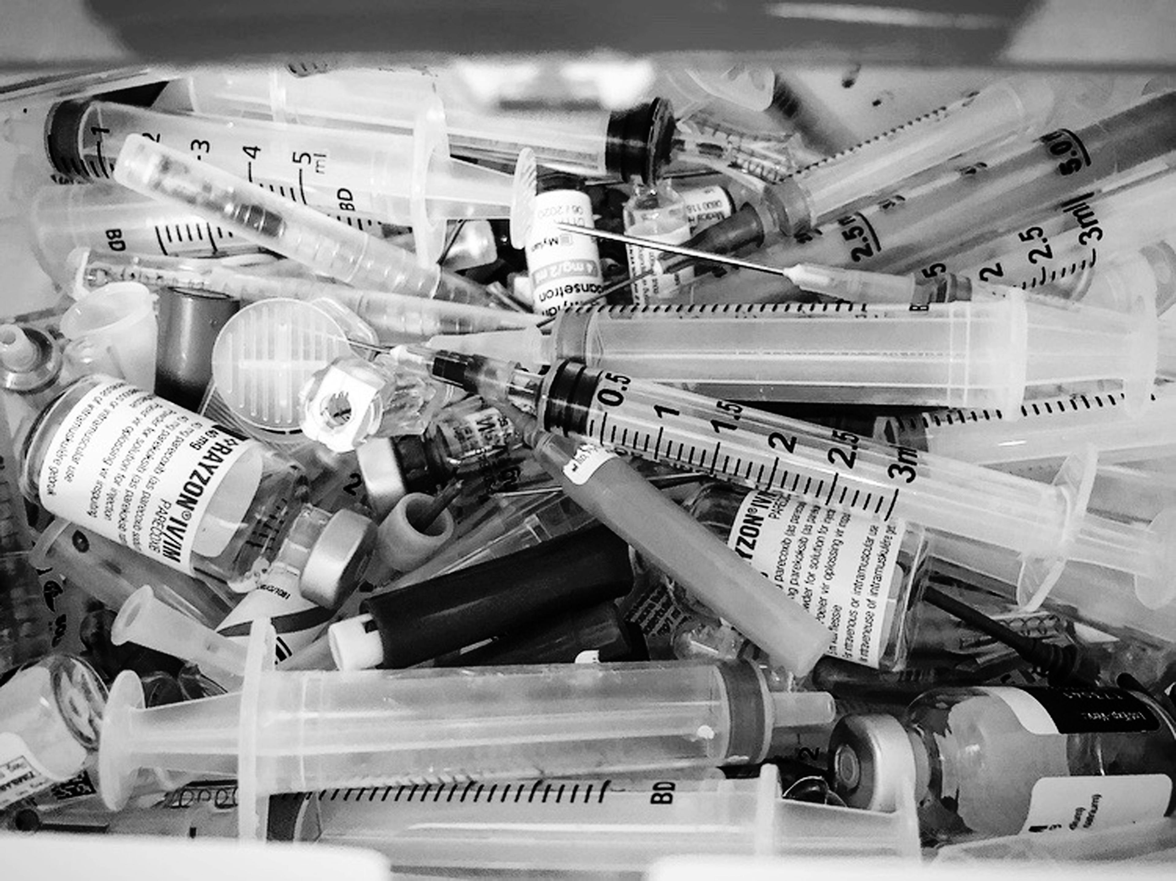 A greyscale collection of empty syringes and medication bottles.