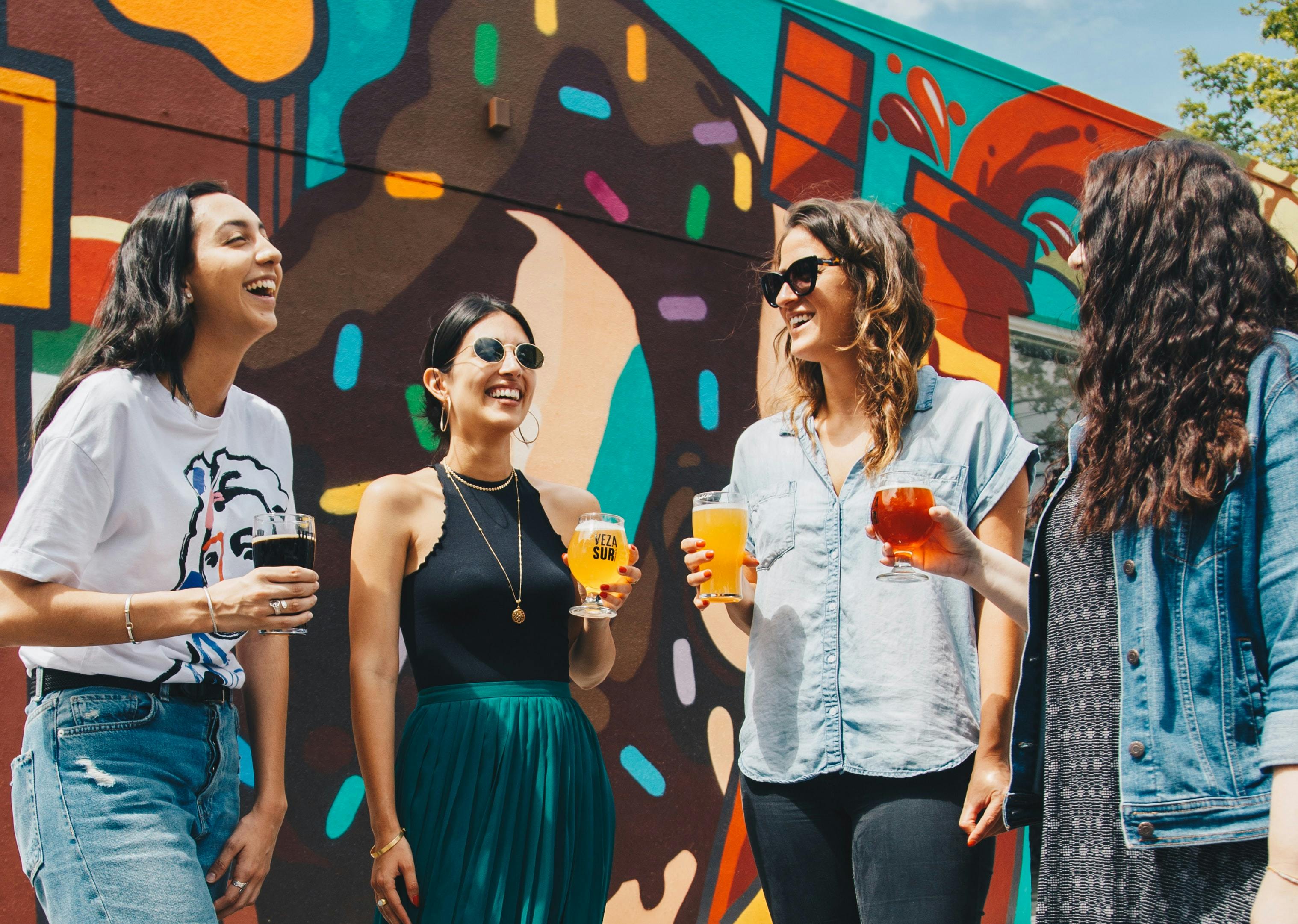 A group of people against a colorful mural, holding drinks and smiling.