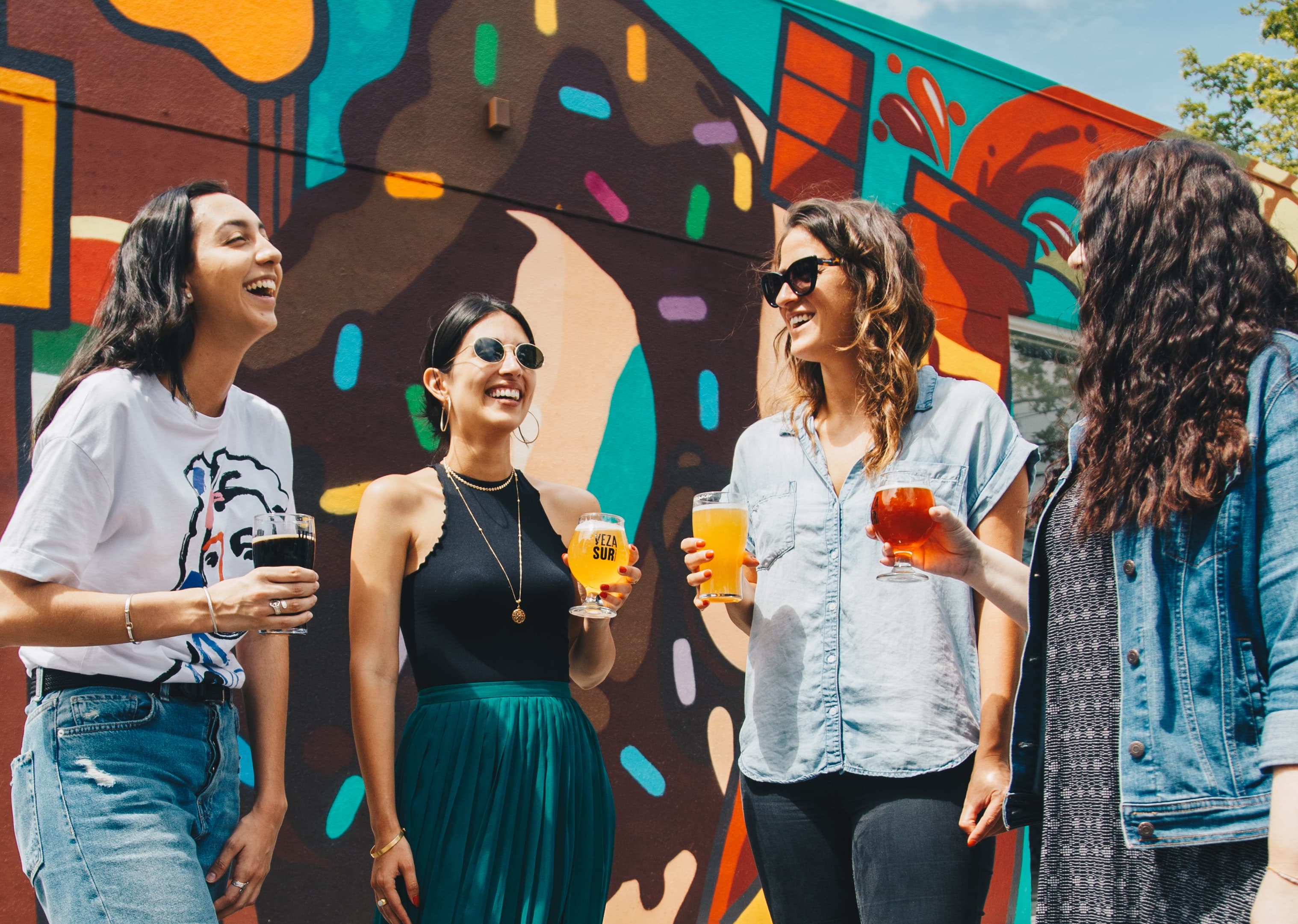 A group of people against a colorful mural, holding drinks and smiling.