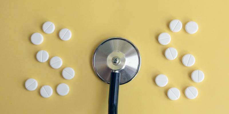 A stethoscope between two lines of white pills against a yellow background.