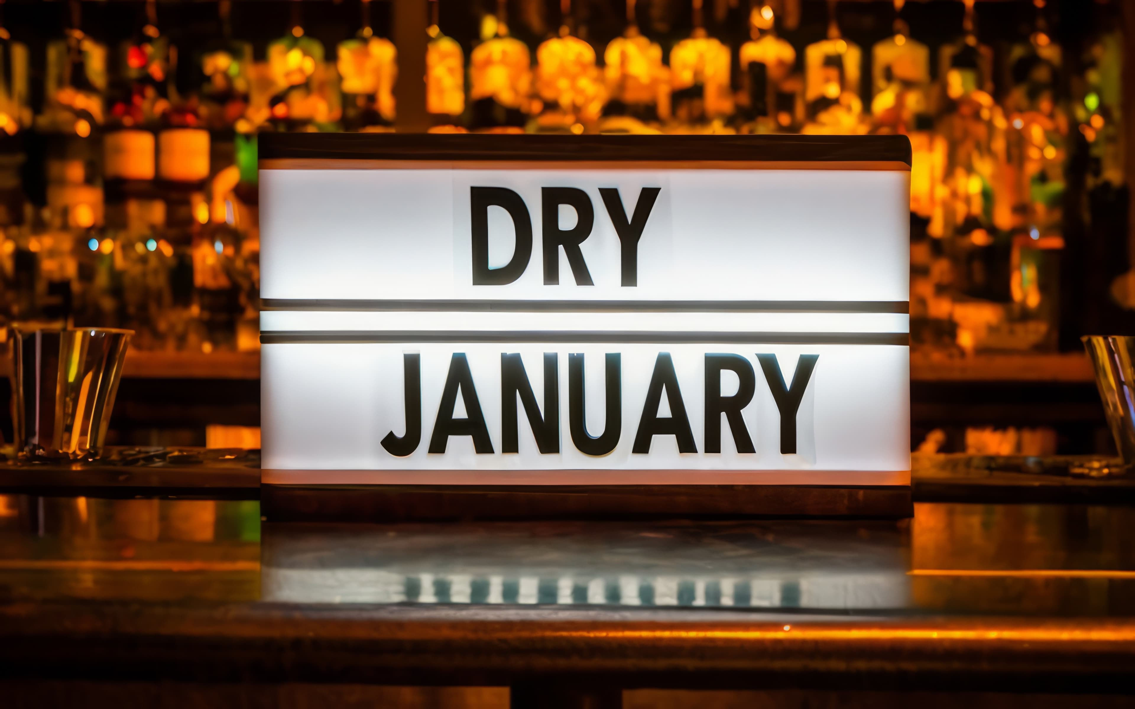 Dry January light box information sign on a bar with booze filled shelves behind it.